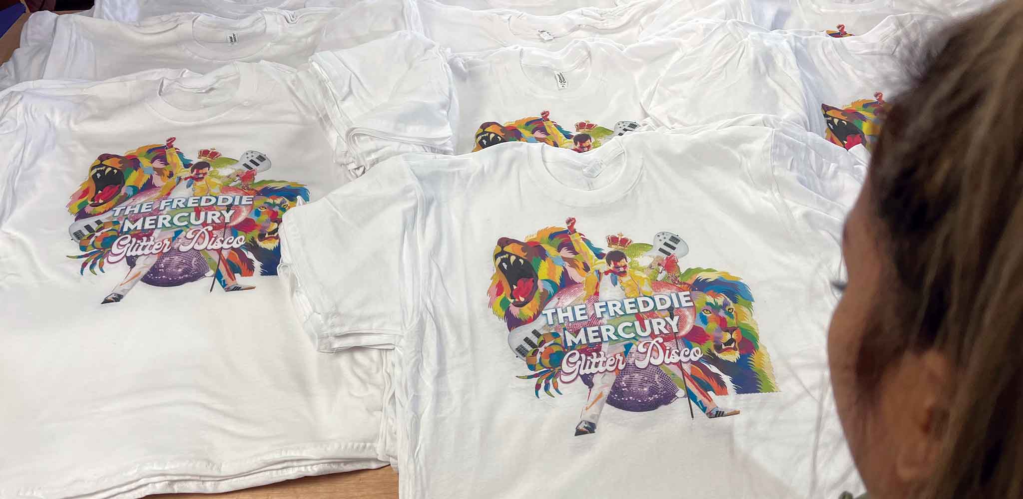 A girl looking over many printed white t-shirts laid out on a table.