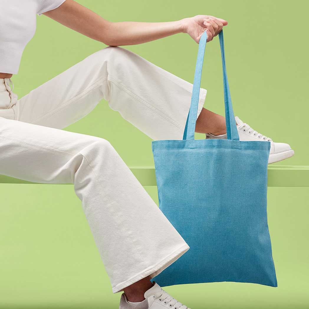 Person holding a blue tote bag against a green background