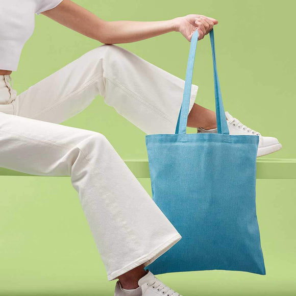 Person holding a blue tote bag against a green background