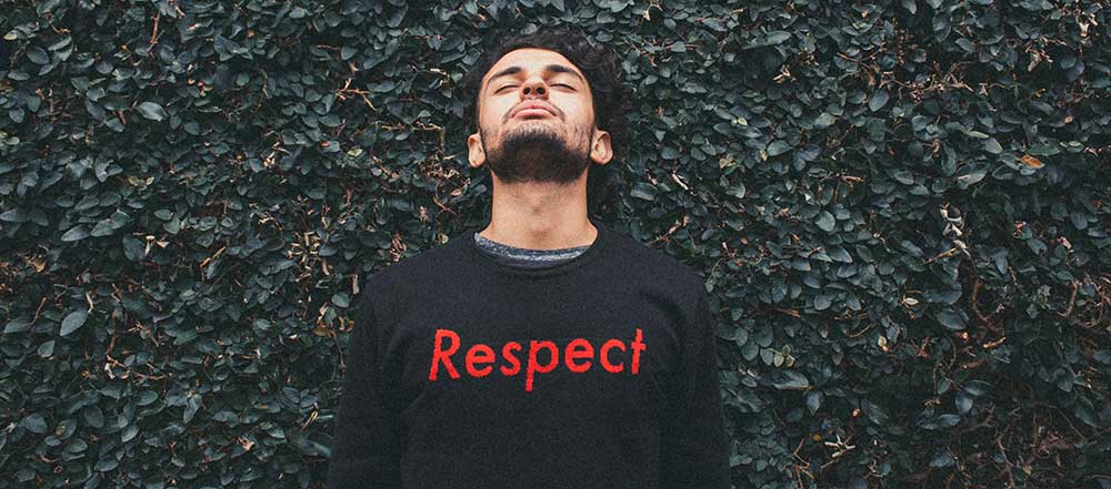 Man wearing a black sweater with 'Respect' in red text against a green leafy background