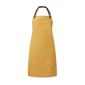 A mustard yellow bib-apron with a leather-like adjustable strap at the neck and a pen pocket on the front. It is displayed against a white background. Premier Annex Oxford Bib Apron - PR144