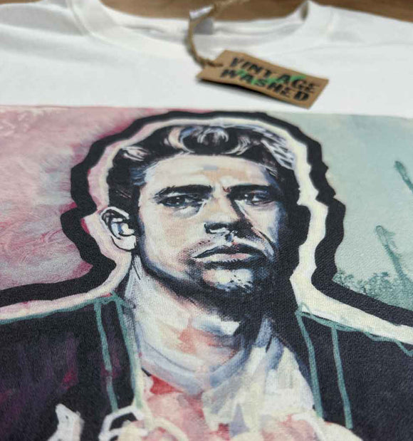 A close-up of a white graphic t-shirt featuring a painted portrait of a man with a 'Vintage Washed' paper tag attached at the collar.