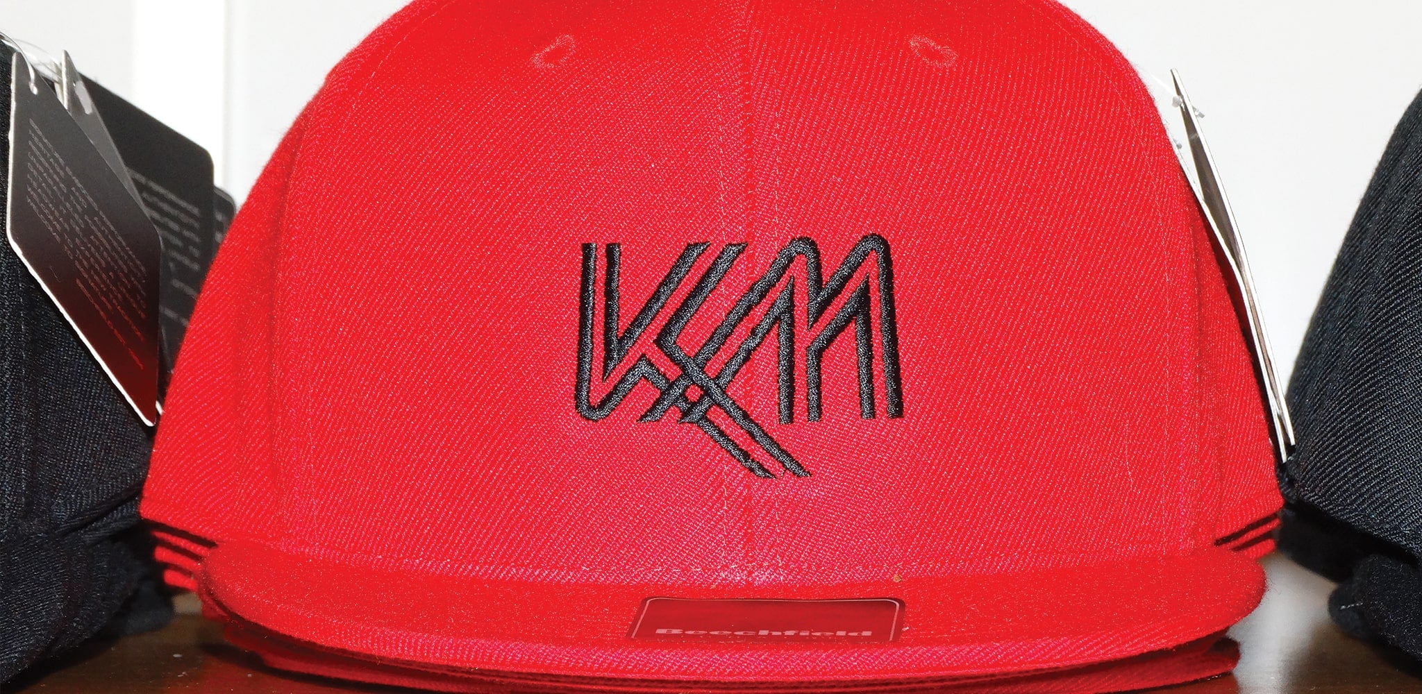 A close up image of a red snapback cap with a black embroidery logo