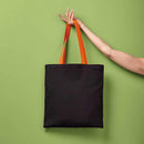 Black tote bag with orange handles held by a hand against a green background