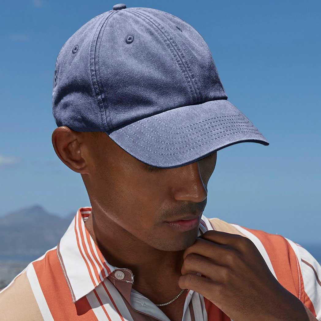 Man wearing a blue cap and striped shirt against a clear blue sky