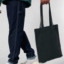 Person holding a black tote bag with a plain background