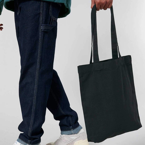 Person holding a black tote bag with a plain background