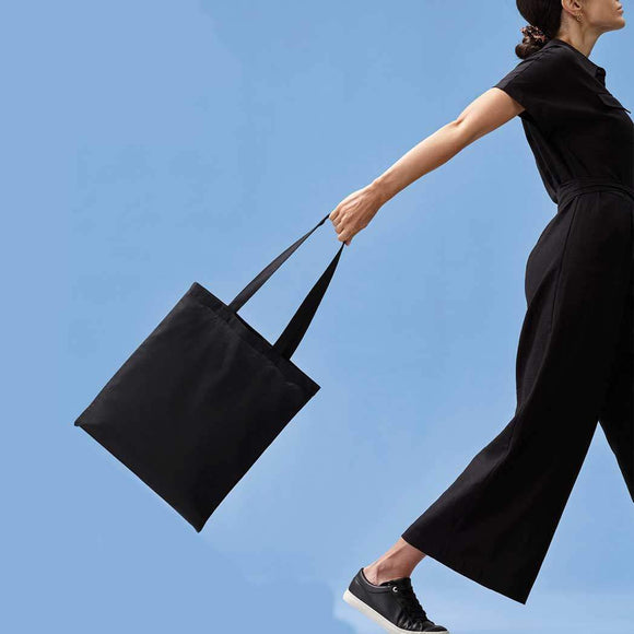 Person holding a black tote bag against a clear blue sky