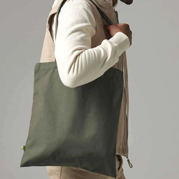 Person holding a green tote bag against a plain background