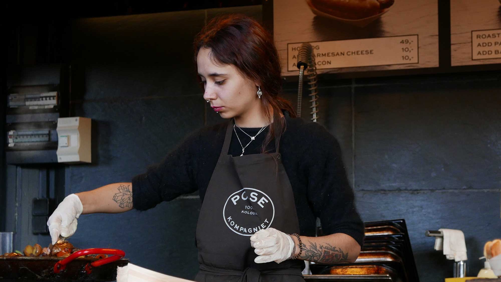 Person wearing a black apron with 'Close' branding in a kitchen setting.