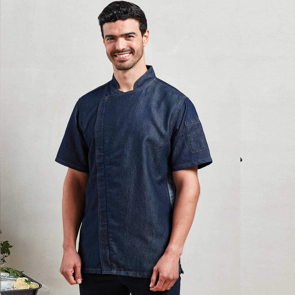 A model wearing a short sleeve indigo denim chef's jacket with a mandarin collar, side vents, and a zip-close front. Premier Chef's Zip-Close Short Sleeve Jacket - PR906