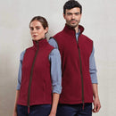 A man and woman with checked shirts and blue pants both wearing Premier Artisan Fleece Gilet - PR803 in burgundy against a light grey background