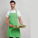 Man wearing a white shirt with an apple green bib apron with front pocket carrying a tray of vegetables. Colours Bib Apron with Pocket - PR154