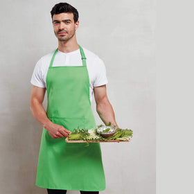 Man wearing a white shirt with an apple green bib apron with front pocket carrying a tray of vegetables. Colours Bib Apron with Pocket - PR154