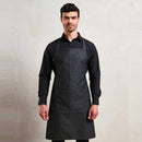 Man wearing a black shirt with a blue denim Bib Apron with Pocket on a light grey background. Denim Bib Apron with Pocket - PR154